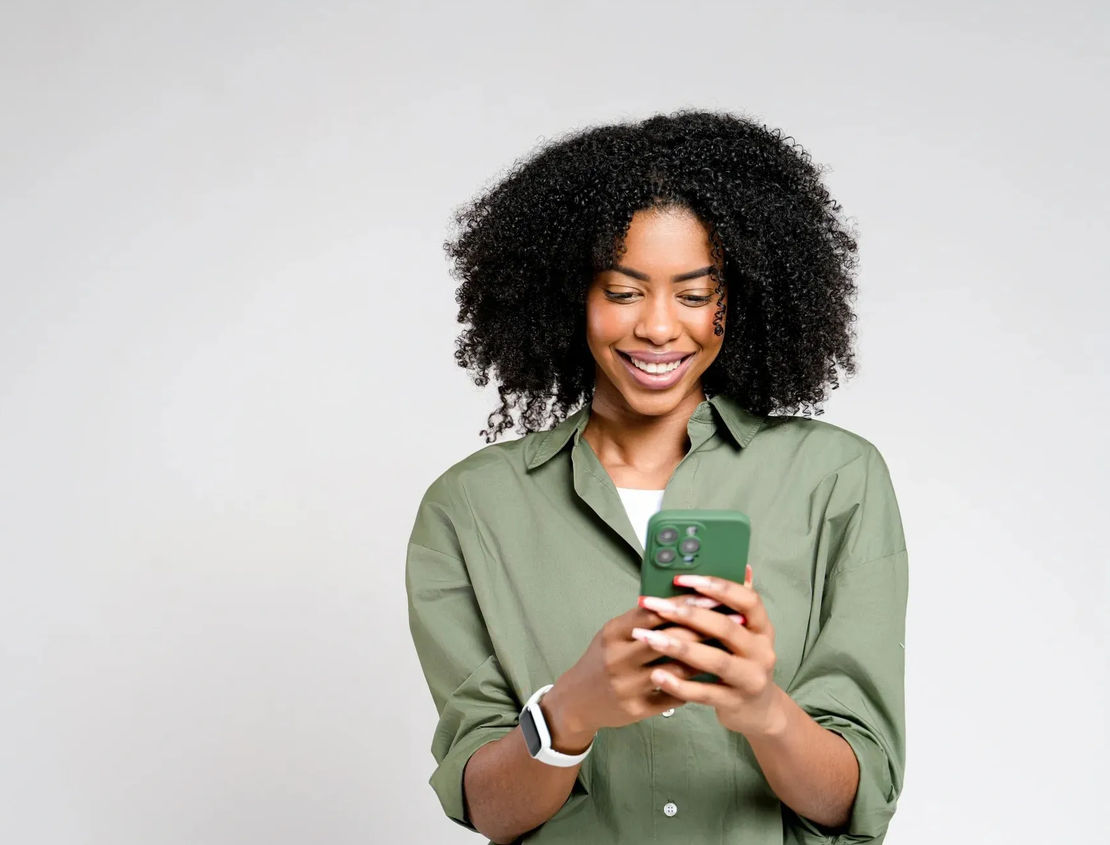 A woman is smiling while looking at her cell phone.