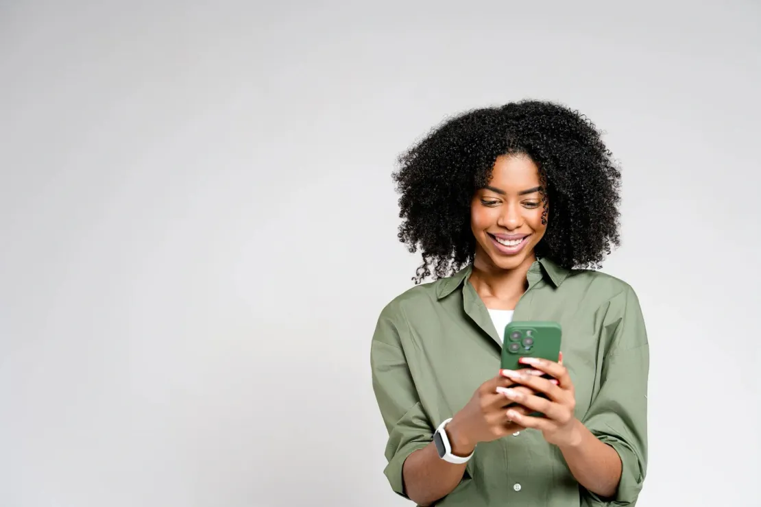 A woman is smiling while looking at her cell phone.