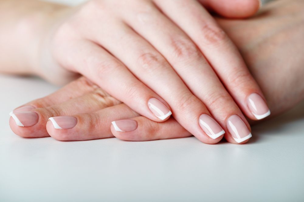 Two hands with pale pink manicured nails resting together on a white surface