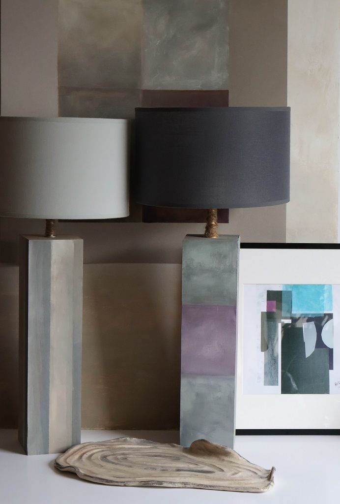 Hay dos lámparas sobre una mesa al lado de un cuadro.