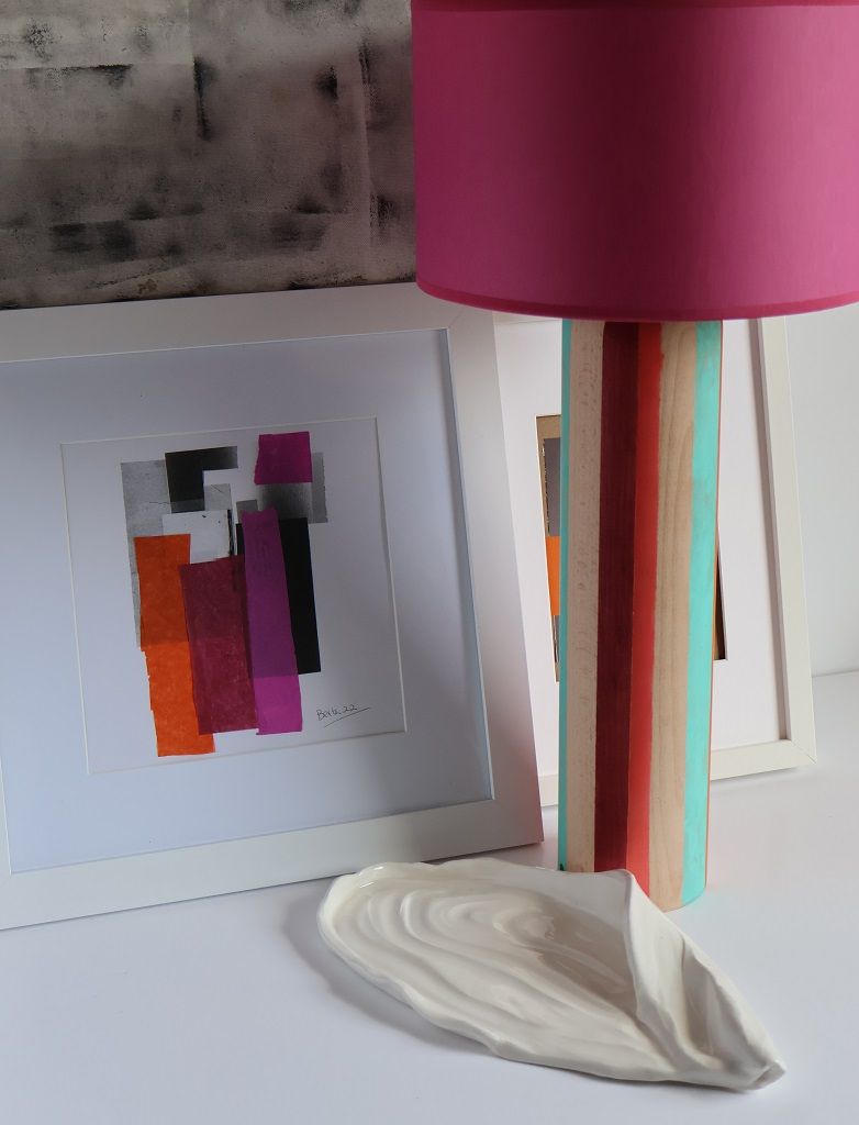 Una lámpara con pantalla rosa se encuentra junto a un cuadro enmarcado.