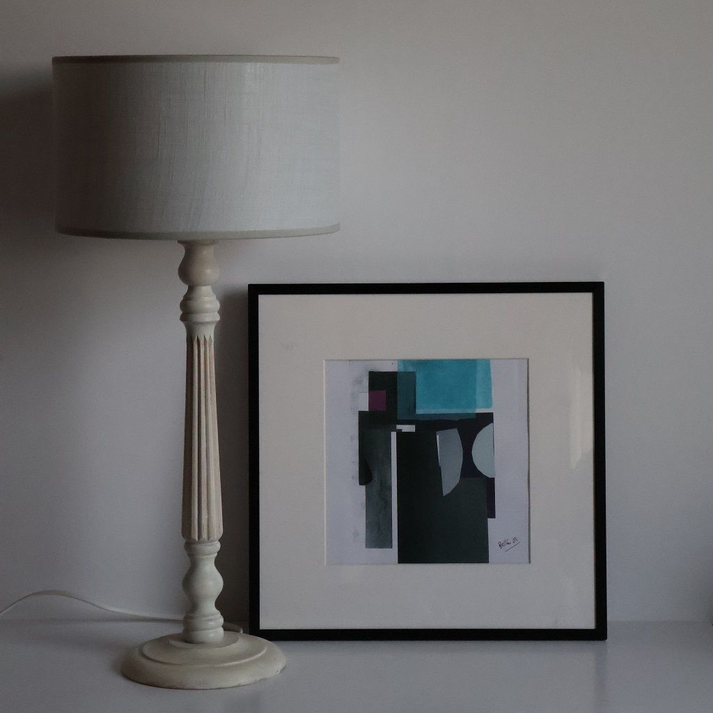 Una lámpara está junto a un cuadro enmarcado sobre una mesa.