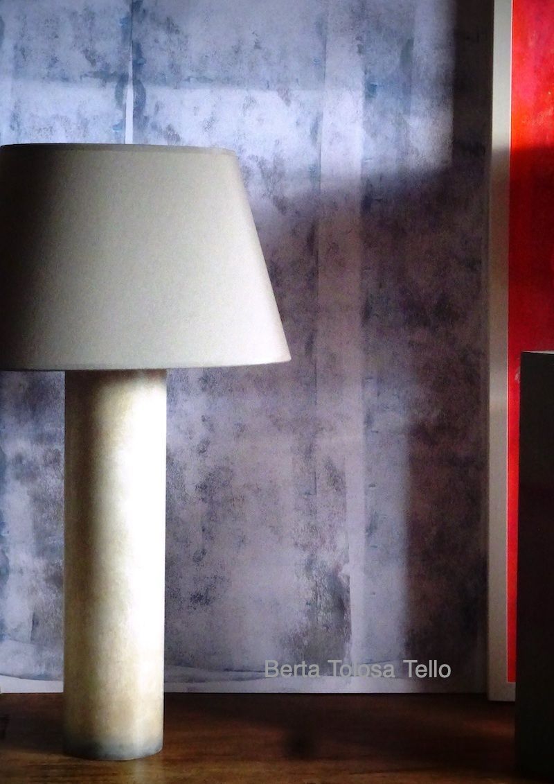 Una lámpara con pantalla blanca se encuentra delante de un cuadro de Petra Bassa Tello.