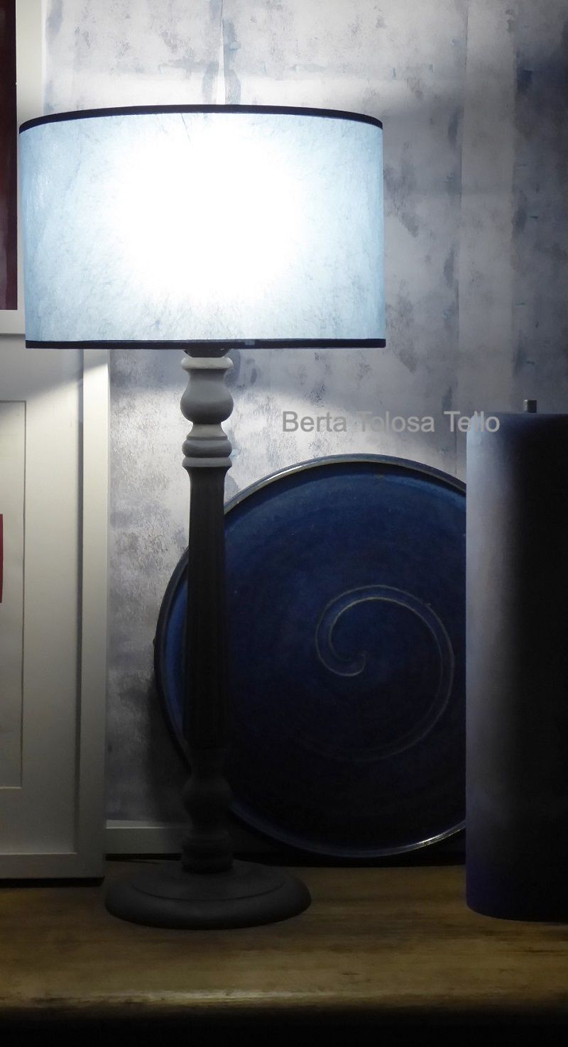 Una lámpara con pantalla azul está sobre una mesa al lado de un plato azul.