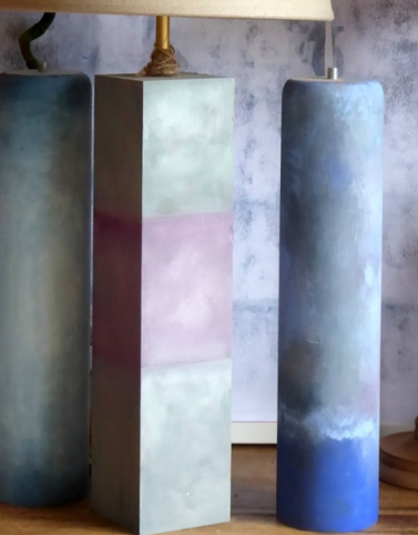 Hay tres velas sobre una mesa al lado de una lámpara.