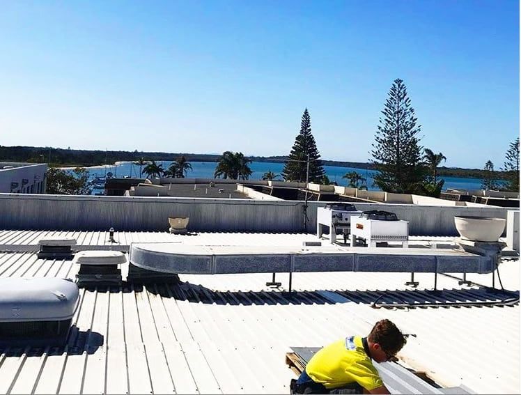 A man is working on the roof of a building - Plumbing and Roofing Port Macquarie NSW