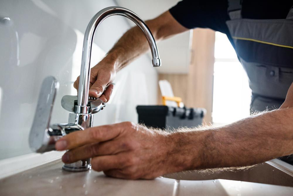 A man is fixing a faucet in a kitchen - Plumbing and Roofing Port Macquarie NSW