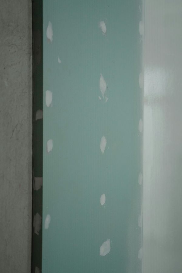 Green wall with white patches, likely filled nail holes, against a gray wall and white door.