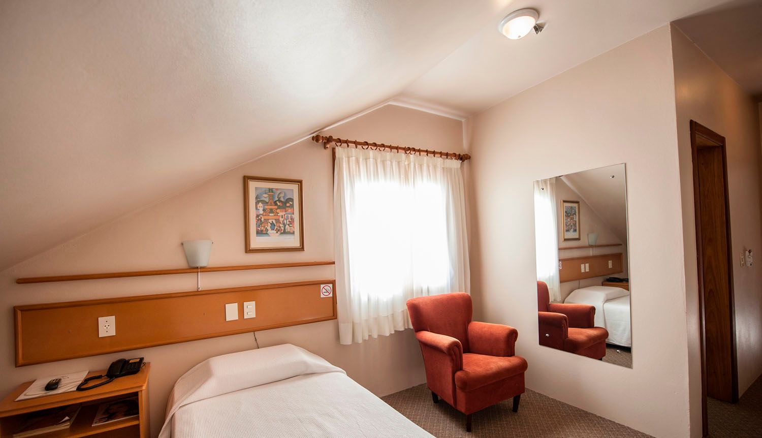 um quarto de hotel com cama, cadeira e espelho.