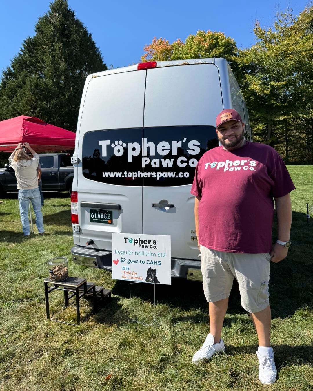 A man in a maroon shirt is standing in front of a white van.