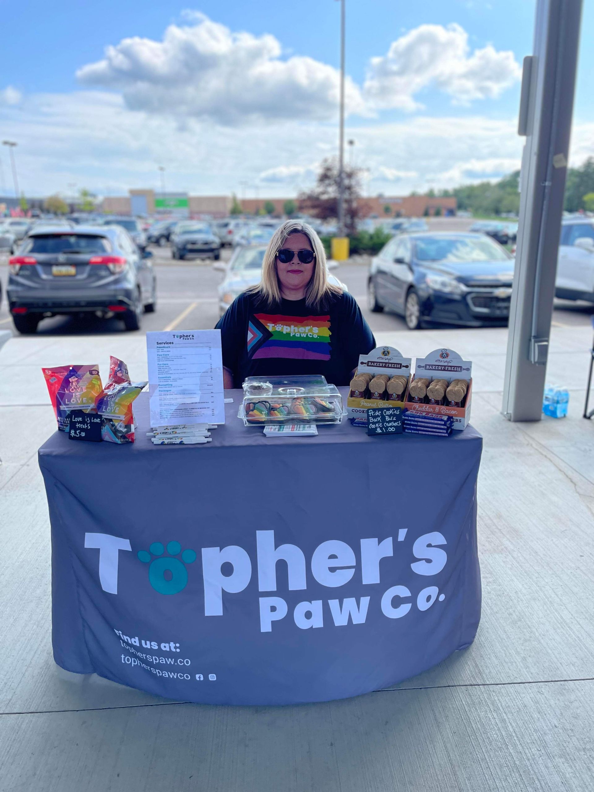 A woman is standing behind a table that says topher 's paw co.