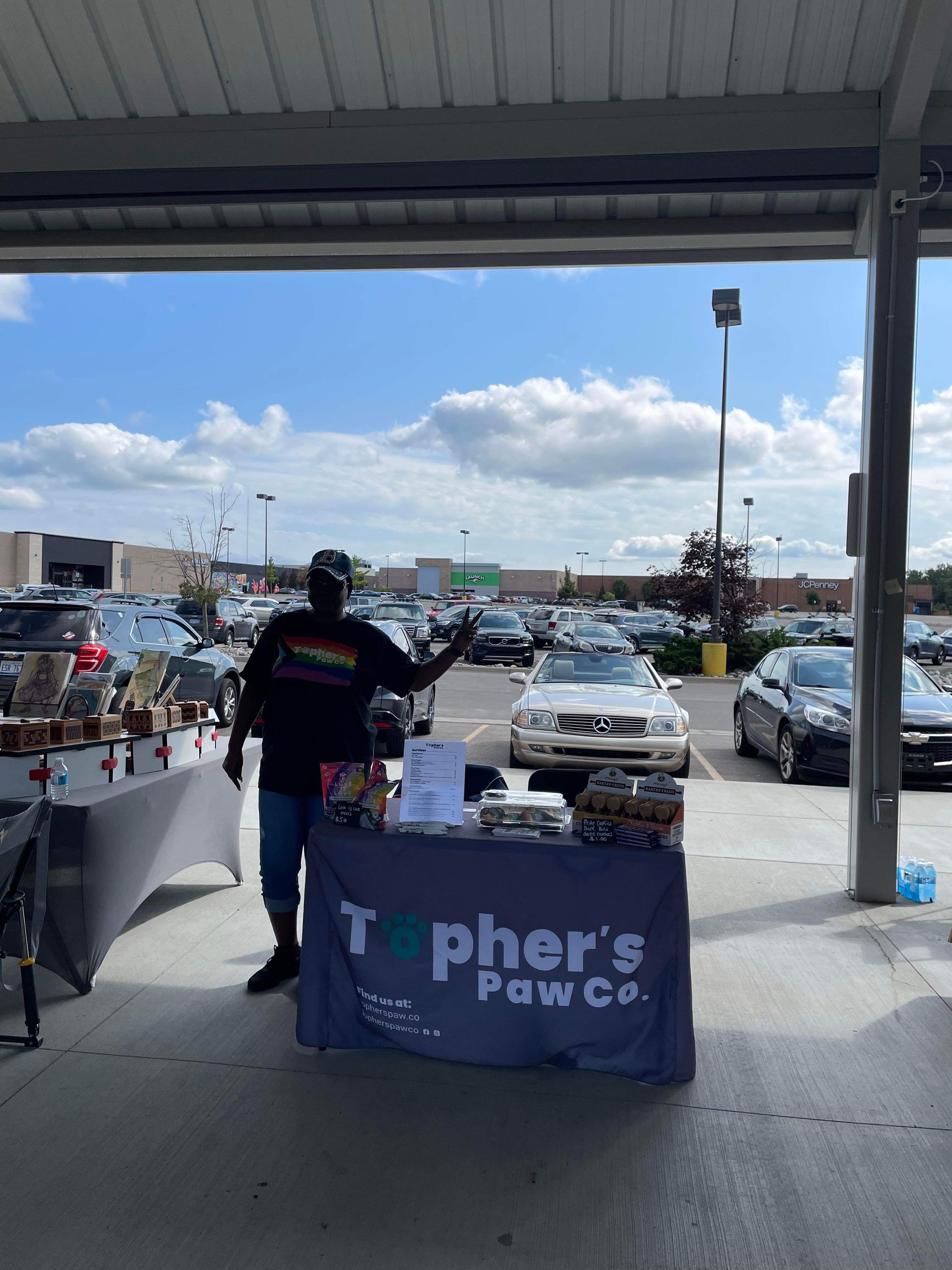 A man stands behind a table that says topher 's paw co.