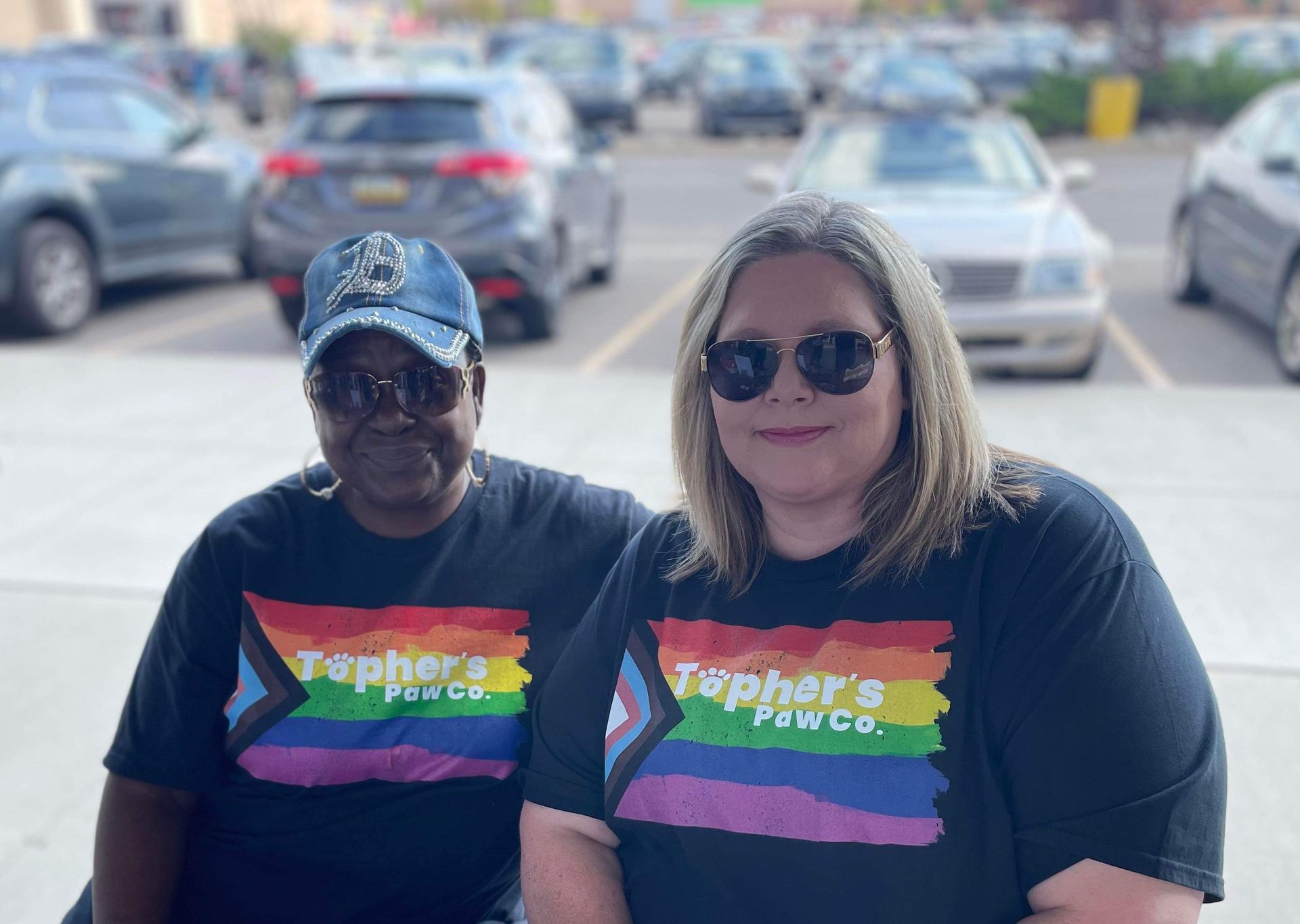 Two women wearing rainbow shirts are sitting in a parking lot.