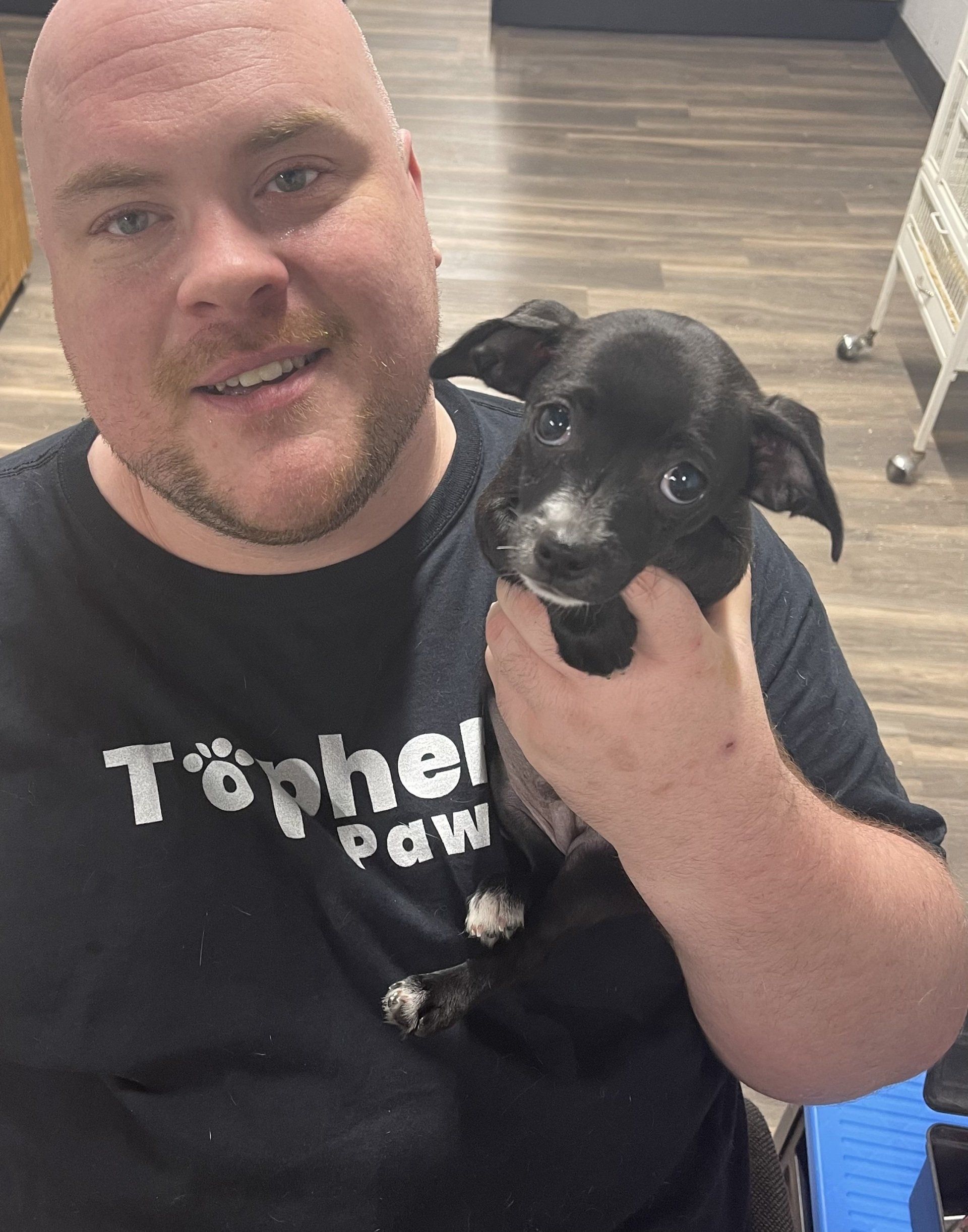 A man is holding a small black dog in his arms.