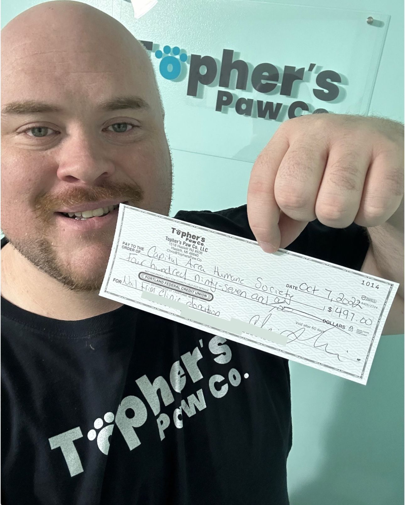 A man in a tipher 's paw co shirt is holding a check