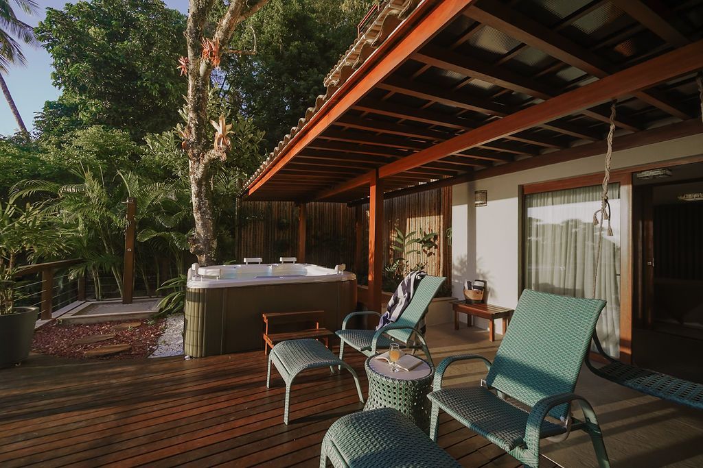 Deck de madeira com banheira de hidromassagem, espreguiçadeiras e pátio coberto. Ambiente tropical, tons naturais de madeira.
