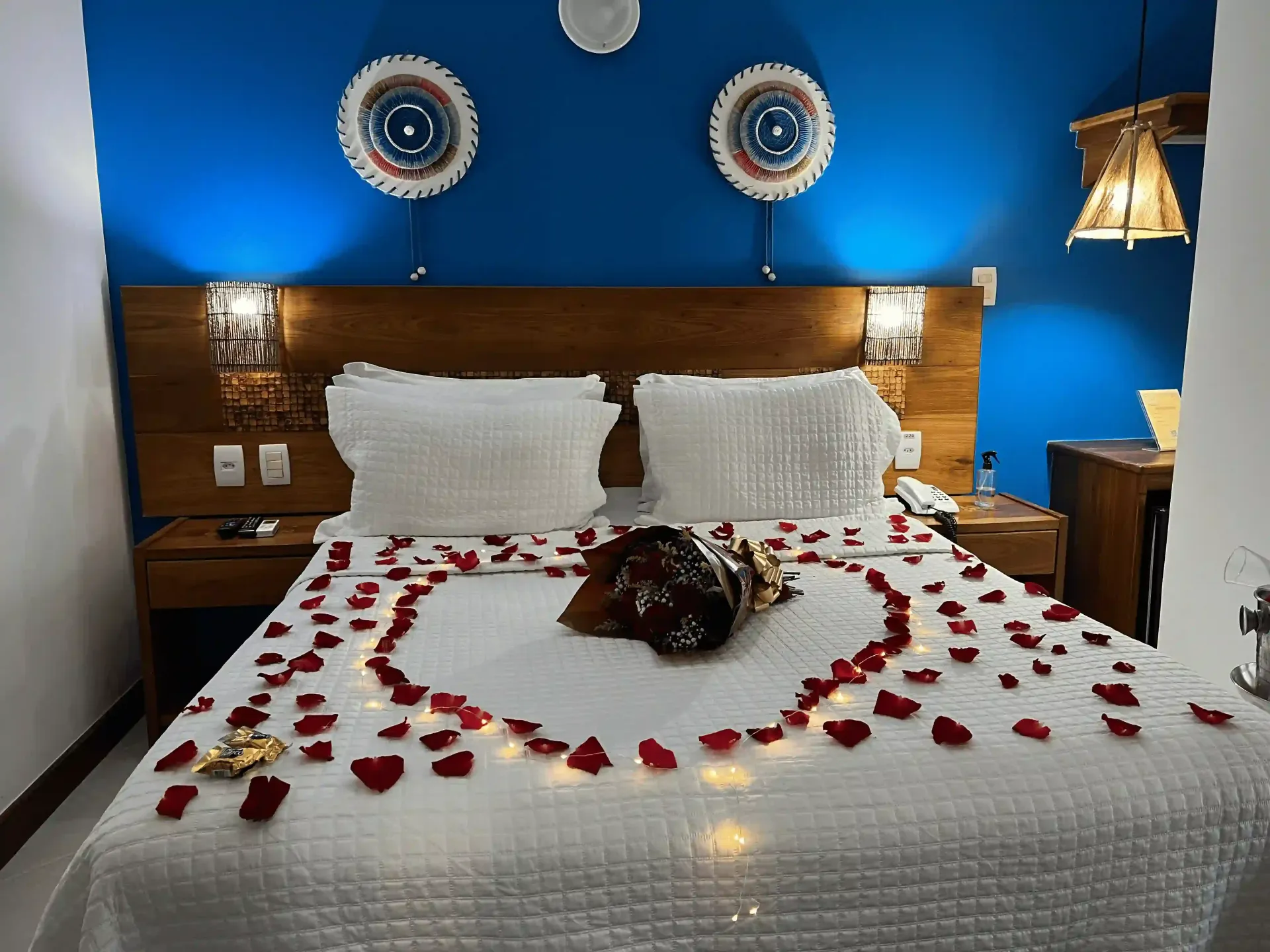 Quarto com cama decorada com pétalas de rosas, cabeceira marrom e paredes azuis.