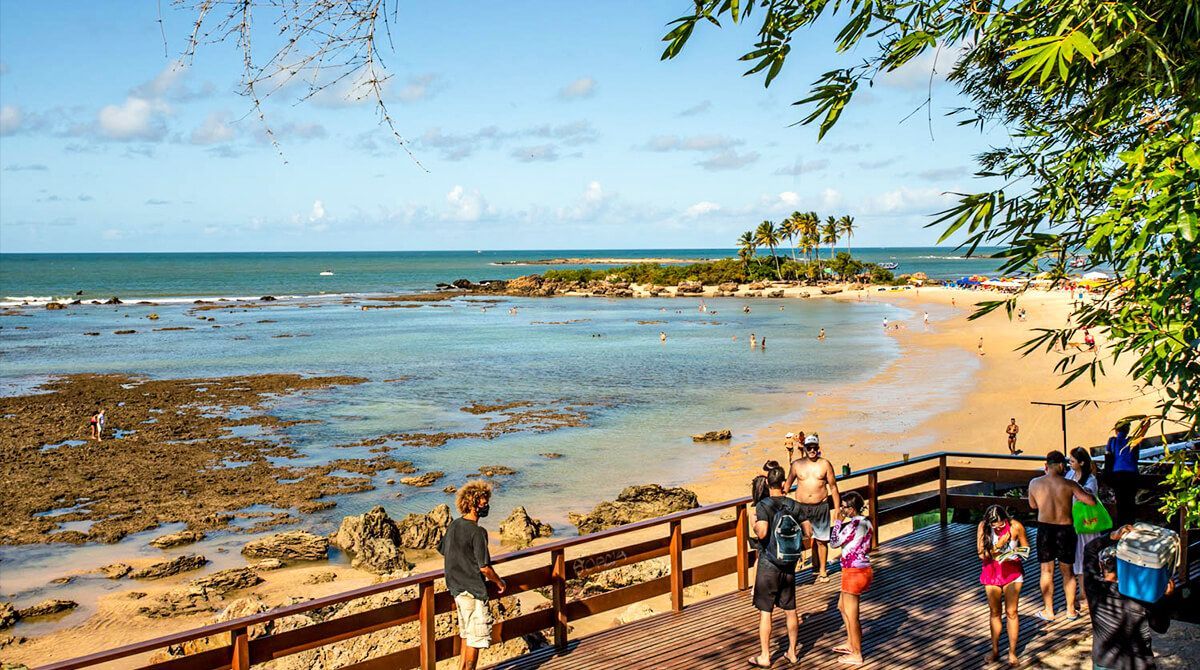 Um grupo de pessoas está em um píer com vista para uma praia. - Pousada Pasargada