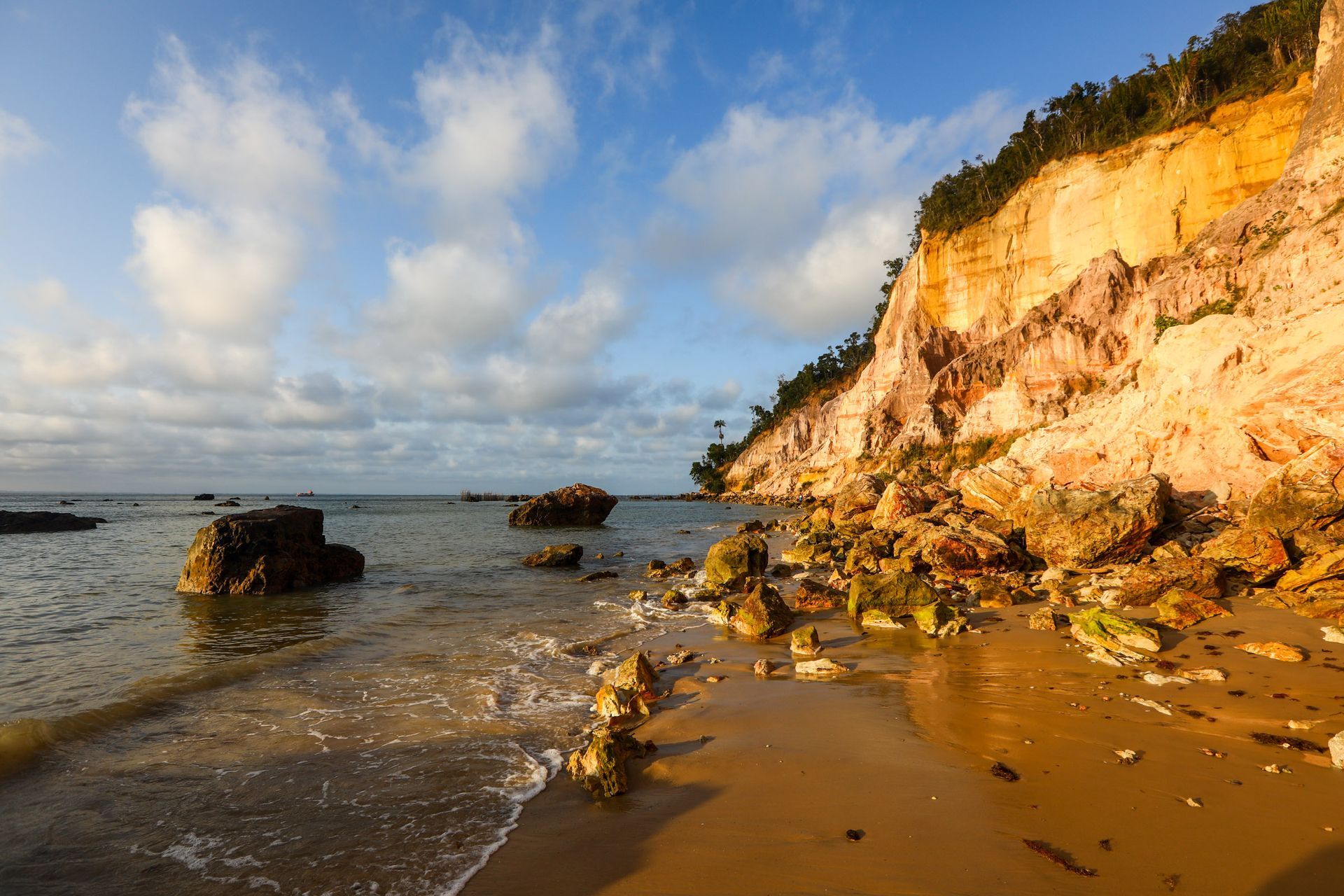 Uma praia com pedras e um penhasco ao fundo - Pousada Pasargada