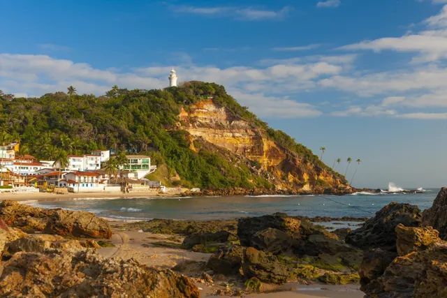 Um farol no topo de uma colina com vista para uma praia. - Pousada Pasargada