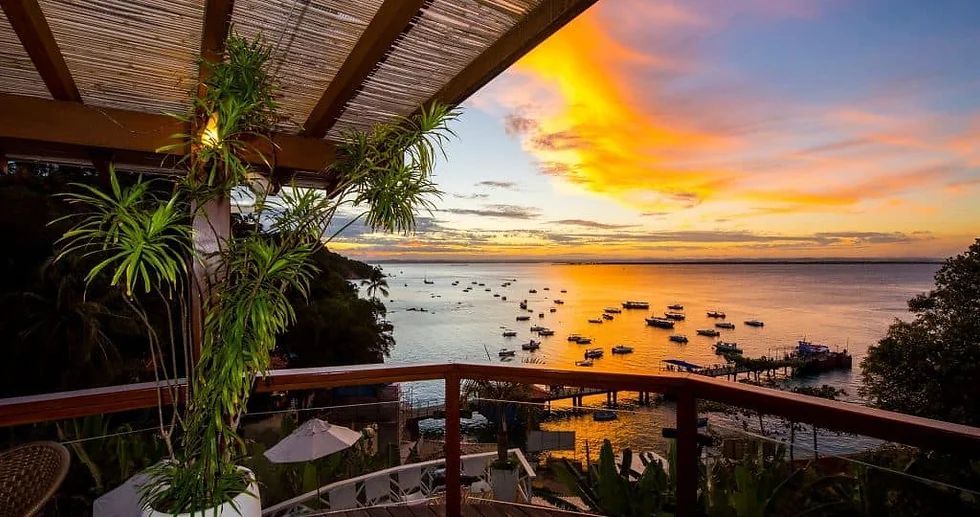 Uma varanda com vista para um corpo de água ao pôr do sol. - Pousada Pasargada