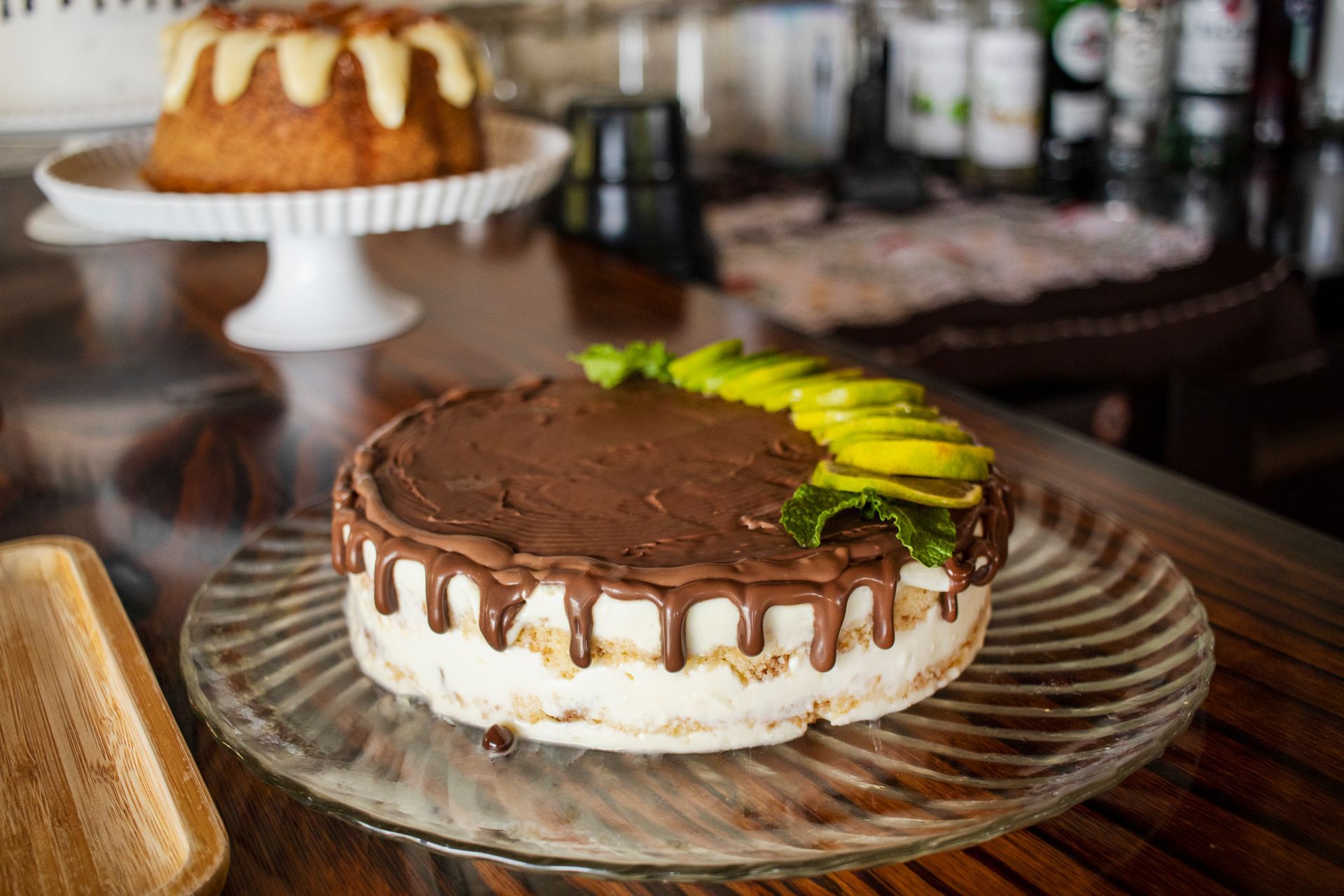 Um bolo está sobre um prato de vidro em cima de uma mesa. - Pousada Pasargada