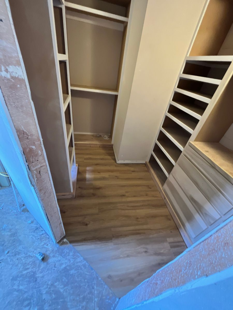 A walk in closet with wooden floors and shelves.