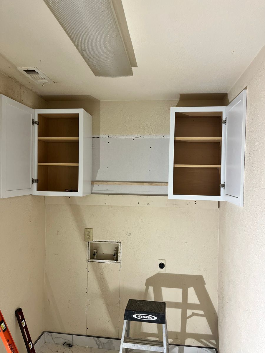 A ladder is sitting in a laundry room with empty cabinets