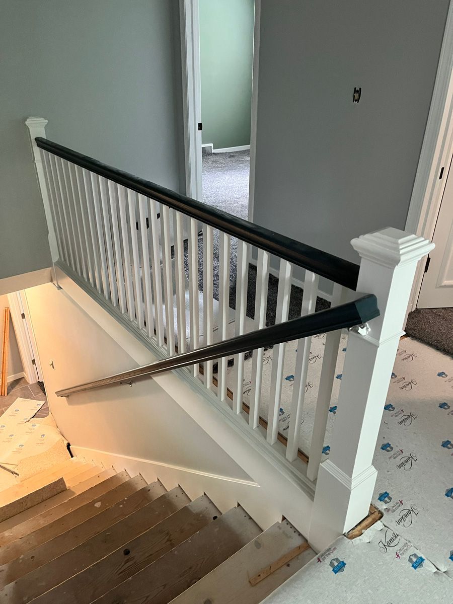 A white staircase with a black railing is being built in a house.