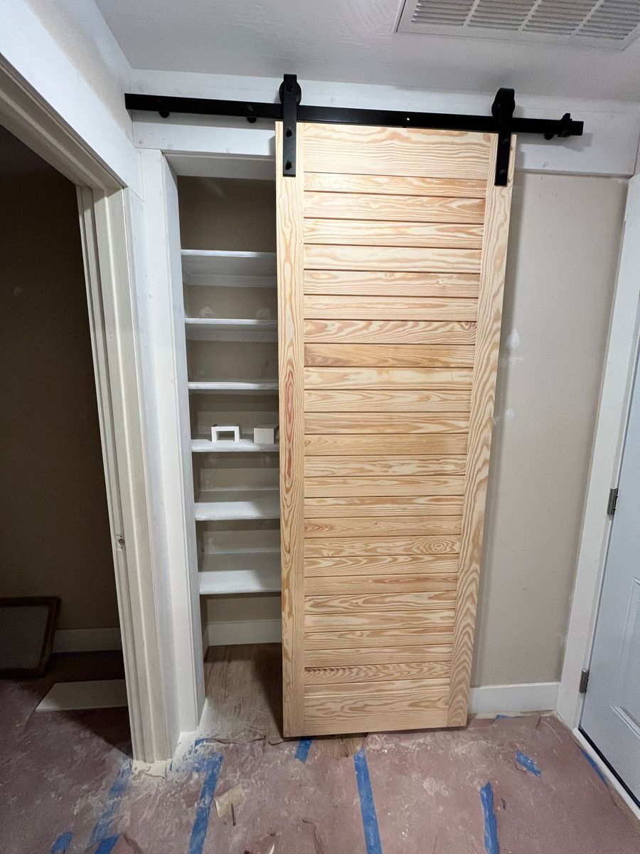 A wooden sliding barn door in a closet with shelves.