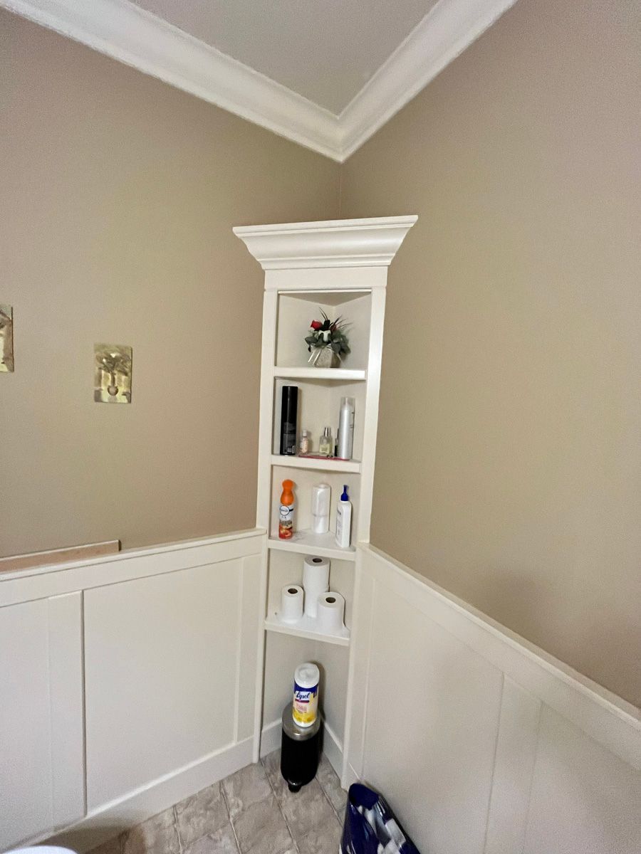 A bathroom with a corner shelf filled with toilet paper