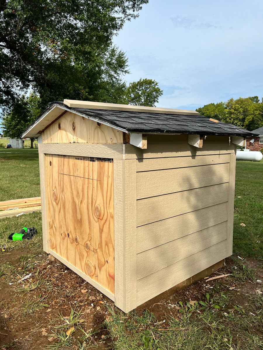 A small wooden shed is sitting in the middle of a grassy field.