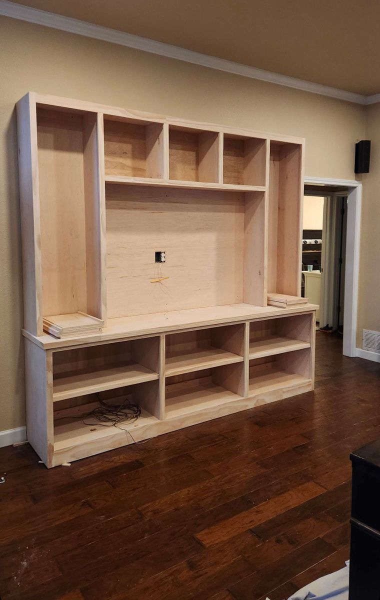 A wooden entertainment center is being built in a living room.