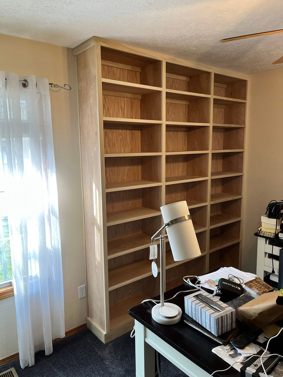 A room with lots of shelves and a desk with a lamp on it