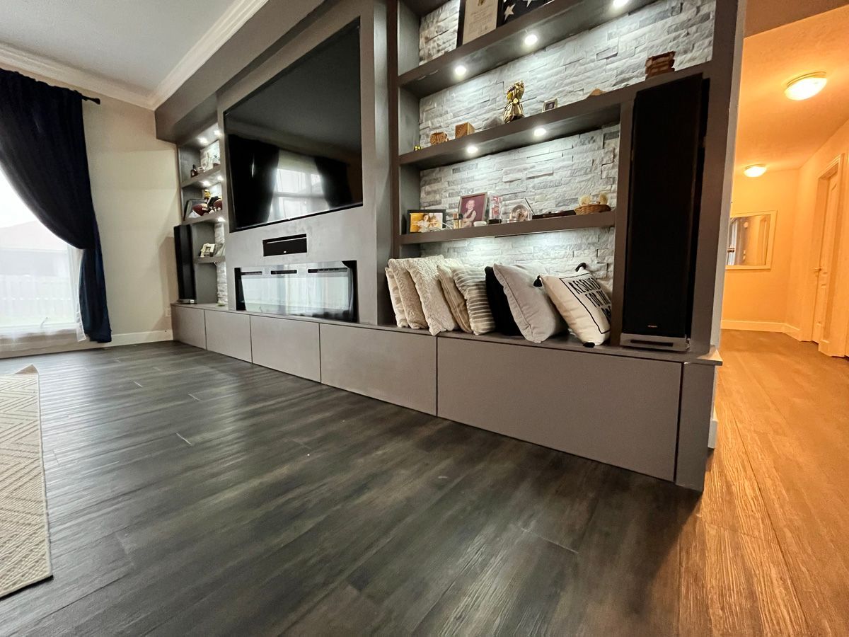 A living room with hardwood floors , shelves , a flat screen tv and a fireplace.