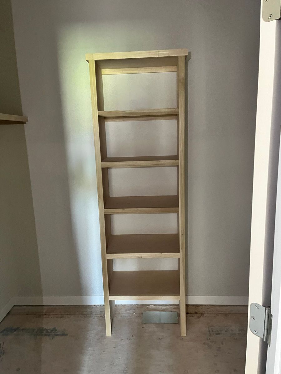 A wooden bookshelf is sitting in a closet next to a door.