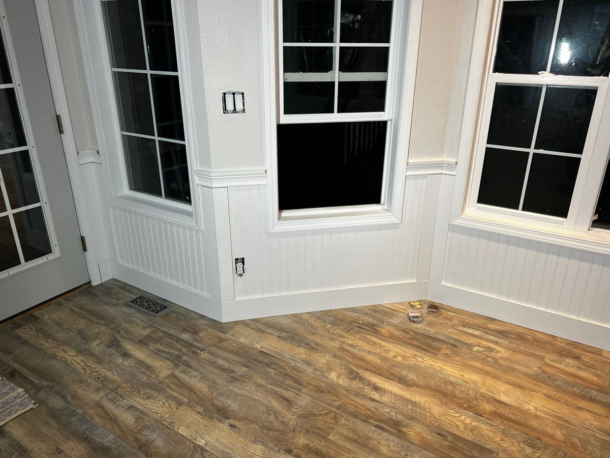 A room with hardwood floors , white trim , and two windows.