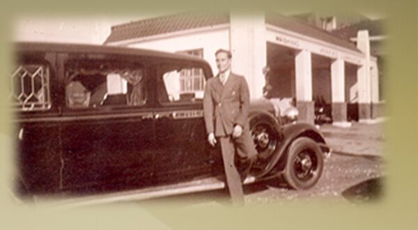 A black and white photo of a man standing next to a car