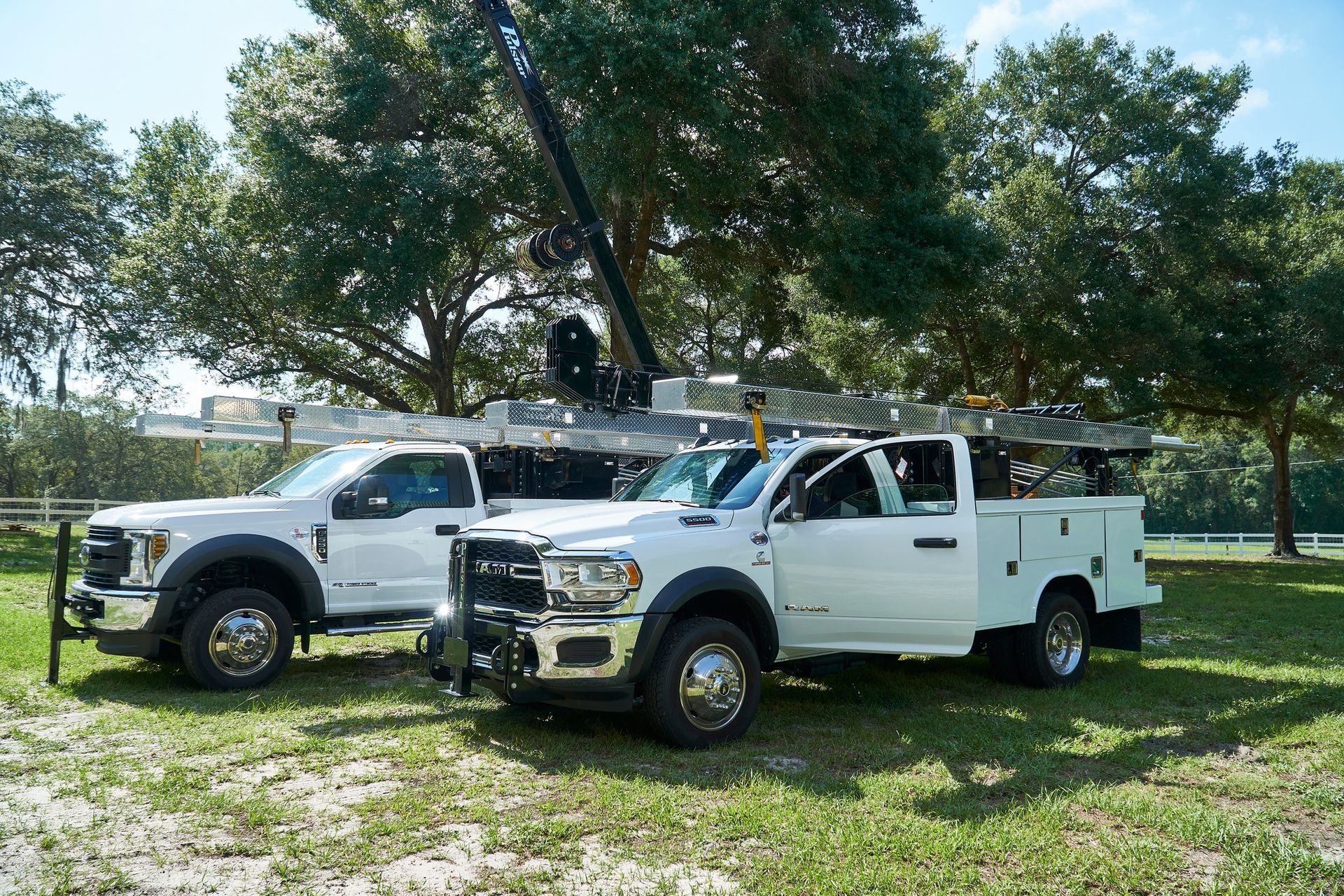 Two white trucks are parked next to each other in a grassy field.