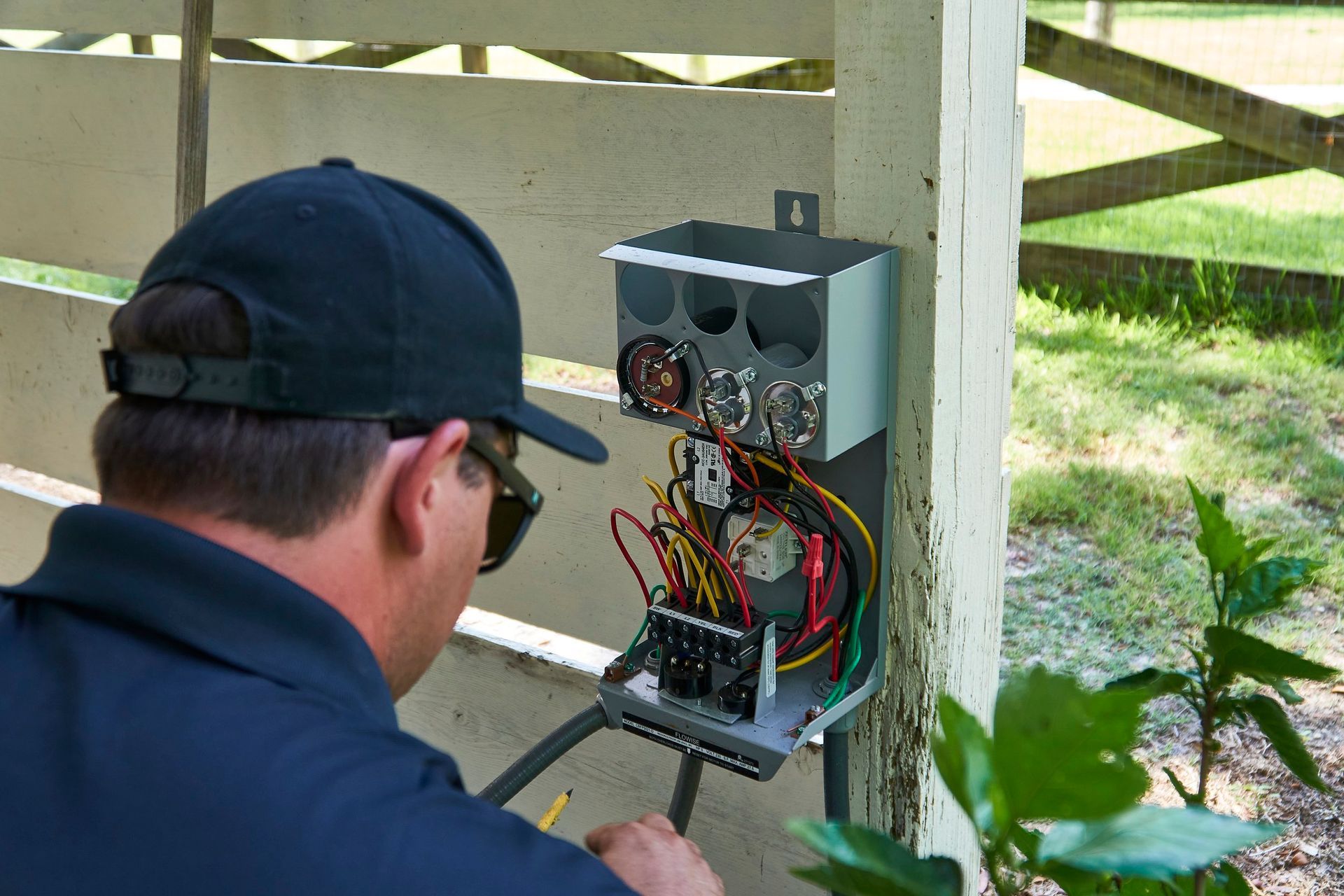 A man is working on an electrical box on a fence.