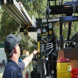 A man in a baseball cap is pointing at a machine.