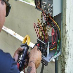 A man is working on an electrical box with a clamp meter.