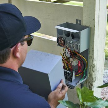 A man wearing a hat and sunglasses is working on an electrical box.