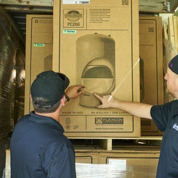 Two men are standing in front of a large cardboard box.