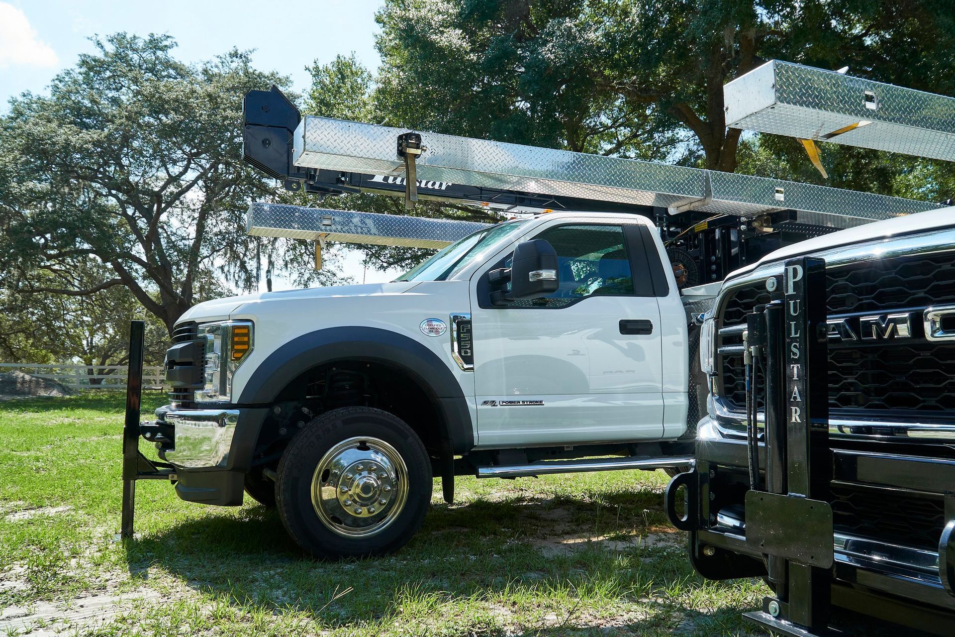 A white truck with a crane on top of it is parked in a grassy field.