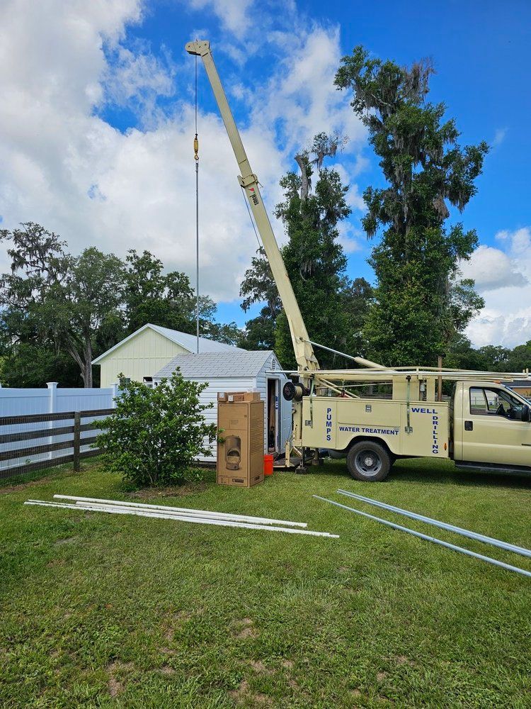 A truck with a crane attached to it is parked in the grass in front of a house.