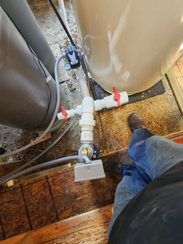 A person is standing on a wooden floor next to a water heater.