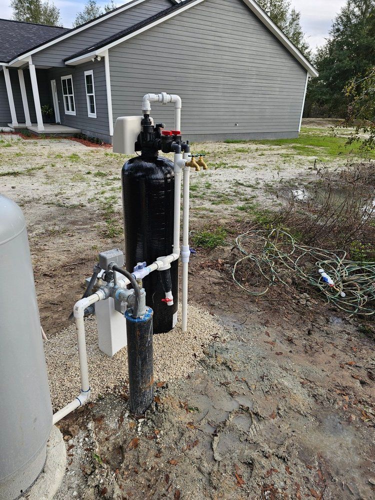 A water filter is sitting in the dirt in front of a house.