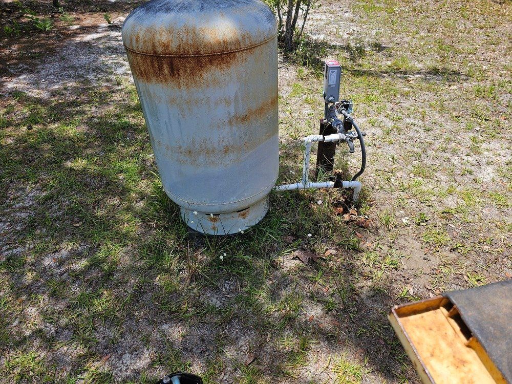 A rusty propane tank is sitting on top of a lush green field.
