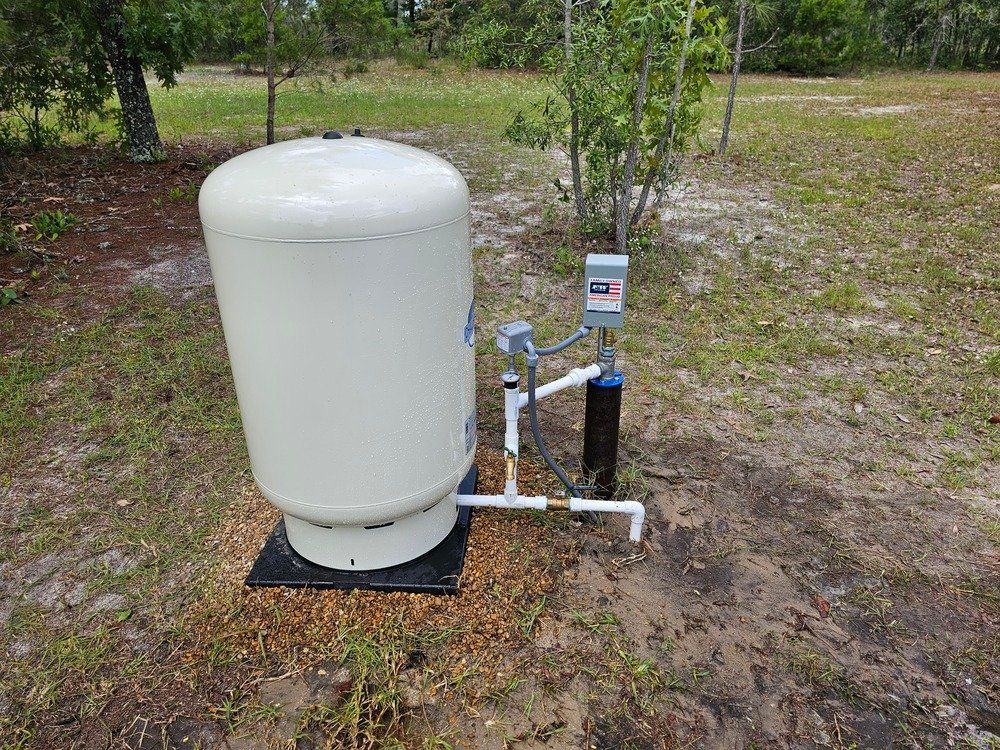 A water tank is sitting on top of a dirt field next to a tree.
